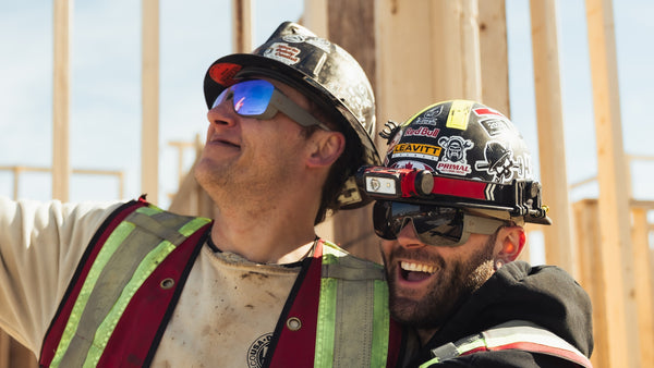 Two construction workers wearing hard hats and safety glasses on a building site.