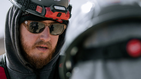 Person wearing a helmet with a light and sunglasses, looking to the side.